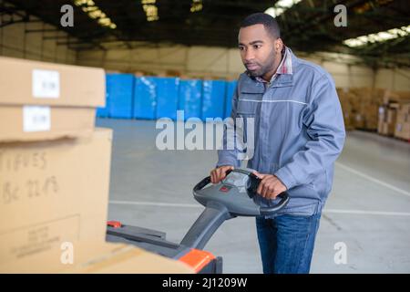 addetto al magazzino che utilizza transpallet elettrico Foto Stock