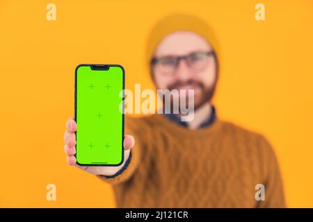 Giovane uomo sorridente caucasico barbuto mostrando la visualizzazione verticale del suo telefono cellulare al fuoco selettivo della fotocamera è sul telefono casual vestiti arancione sfondo isolato studio shot . Foto di alta qualità Foto Stock