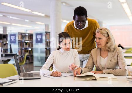 Tutor femminile che aiuta gli studenti a prepararsi per l'esame in biblioteca Foto Stock