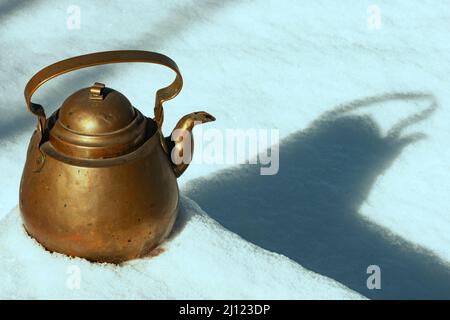 Terreno nevoso con linee e lunghe ombre che mettono in risalto un antico teakettle in rame metallico alla luce del sole sui gradini. Spazio di testo disponibile. Foto Stock