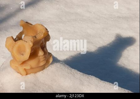 La figura della cera di una testa o di un angelo si appoggia su terra nevosa che getta una lunga ombra. Gli occhi sono chiusi in una posa premurosa. Spazio di testo disponibile. Foto Stock