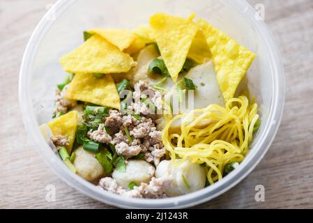 Spaghetti secchi palle di maiale palle di pesce e maiale tritato con wonton croccanti e verdure in una ciotola di plastica su tavola di legno, vista dall'alto Thai e Cina Asian foo Foto Stock