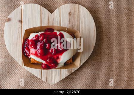 Rotolo di cannella Frosted Cherry da vicino su un pannello a forma di cuore in legno, piatto con spazio copia Foto Stock