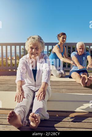 L'aria fresca e l'esercizio fisico sono buoni per il corpo. Shot di una coppia anziana che fa yoga con un istruttore sul loro patio esterno. Foto Stock