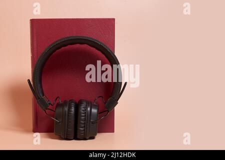 Audiolibro. Le cuffie si posizionano accanto a un libro su uno sfondo colorato Foto Stock