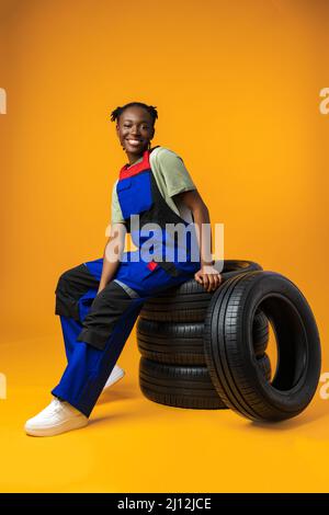 Ritratto di mechanic femminile nero sorridente in posa con pneumatici auto nuovi in studio Foto Stock