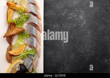 Aringa sottaceto con patate al forno, cipolle e lattuga, su sfondo scuro Foto Stock