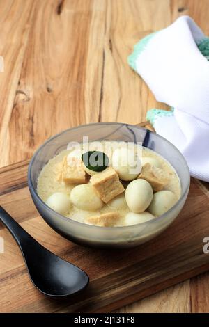 Opor Tahu Telur Puyuh o curry indonesiano con tofu e uovo di quaglia, servito su ciotola di ceramica, su tavola di legno Foto Stock