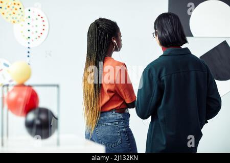 Vista posteriore di giovani e donne etnicamente diversi che guardano la pittura astratta e ascoltano il tour audio alla mostra nella galleria d'arte Foto Stock