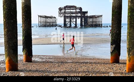 Brighton UK 22nd Marzo 2022 - i corridori passano dal Molo Ovest di Brighton in una bella mattinata di sole a bassa marea come il tempo caldo di sole è previsto per continuare in tutta la Gran Bretagna con temperature che raggiungono gli adolescenti alti nel sud-est: Credit Simon Dack / Alamy Live News Foto Stock