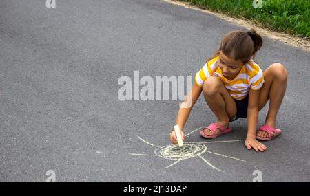 il bambino disegna con gesso sul marciapiede, il cuore è il sole. Natura. Fuoco selettivo Foto Stock