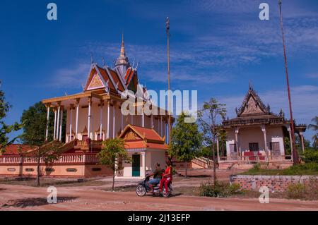 Una coppia cambogiana in moto passa davanti ad un complesso di templi buddisti sulla riva del fiume Tonle SAP. Kampong Chhnang City, Cambogia. © Kraig Lieb Foto Stock