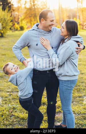 Ritratto di una famiglia felice di tre membri, camminano insieme nel parco e comunicano. Mano di presa. Vacanze estive. Cura della famiglia. Foto Stock