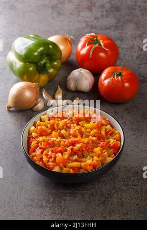 Salsa mediterranea a base di peperoni maturi, pomodori, aglio e cipolle da vicino in un piatto sul tavolo. Verticale Foto Stock