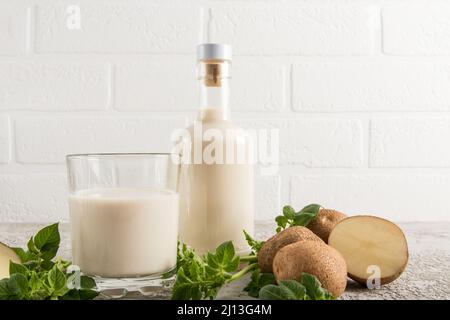 Il latte vegetale vegano dalle patate è una nuova tendenza nel cibo. Bottiglia di vetro del latte di fronte ad una parete bianca del mattone Foto Stock