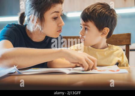 Madre che corregge l'errore fatto da suo figlio nelle lezioni domestiche. Studiare, fare i compiti. Insegnamento online. Formazione online. Foto Stock