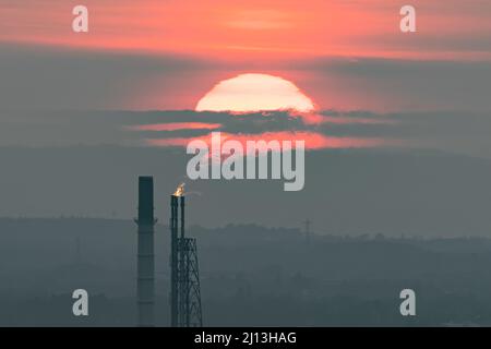 Una quantità di emissioni si riversa fuori dalla catasta di fiaccole di Stanlow a Ellesmere Port contro un tramonto nebuloso, mentre i prezzi del carburante continuano ad aumentare. Regno Unito, marzo 2022 Foto Stock