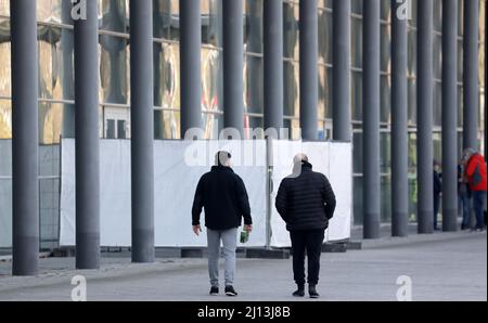 Rostock, Germania. 22nd Mar 2022. Due uomini camminano oltre una recinzione di privacy di fronte all'Hansemesse. Fino ad oggi, l'Hansemesse era il punto di contatto centrale per i rifugiati ucraini nel Meclemburgo-Pomerania occidentale. Ora la struttura iniziale di accoglienza dello stato di Meclemburgo-Pomerania occidentale a Stern Buchholz è quella di assumere questo compito perché la registrazione dei rifugiati all'Hansemesse non può essere gestita senza problemi. Credit: Bernd Wüstneck/dpa-Zentralbild/dpa/Alamy Live News Foto Stock