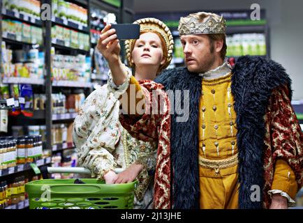 Non troppo reale per fare shopping. Un re e una regina che prendono un selfie nel loro supermercato locale. Foto Stock