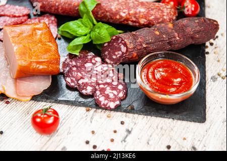 Salsiccia affumicata, carne, pancetta con basilico e pomodori ciliegini Foto Stock