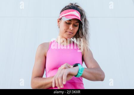 Una giovane ragazza sportiva guarda un orologio intelligente sulla sua mano e controlla il suo polso, prende una pausa dopo il jogging. Foto Stock