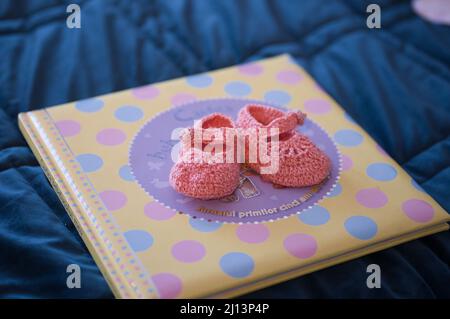 Primo piano di un bambino rosa pastello Booties in cima ad un album fotografico su una coperta blu Foto Stock