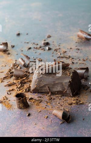 Un blocco di cioccolato con scaglie di cioccolato e polvere di cacao sparsi intorno. Foto Stock