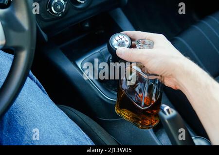 Primo piano dell'uomo che guida l'auto e che tiene una bottiglia di alcool. Guida responsabile e sicura. Foto Stock