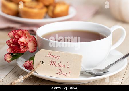 Happy Mothers giorno tag e tazza di tè con garofano rosso su un tavolo di legno Foto Stock