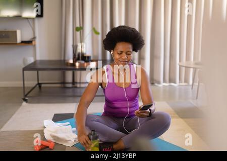 Donna afroamericana medio adulta che usa lo smartphone mentre pratica lo yoga a casa Foto Stock