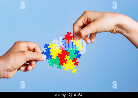 Concetto di giornata di consapevolezza autismo mondiale. I bambini hanno le mani che tengono il cuore colorato del puzzle su sfondo blu Foto Stock