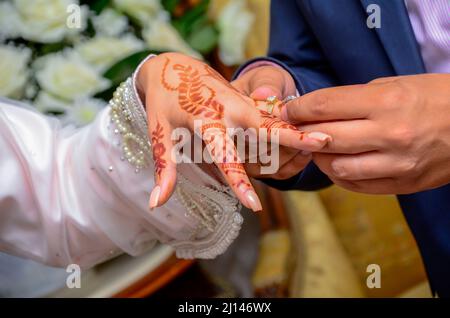 Lo sposo arabo indossa l'anello di nozze della sposa. La mano della sposa è tatuata con henné Foto Stock