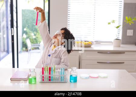 Ragazzo ispanico che analizza la sostanza chimica in provetta mentre fa ricerca scientifica a casa Foto Stock