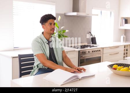 Uomo cieco ispanico che legge libro con braille mentre si siede in cucina a casa Foto Stock