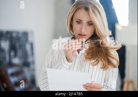 Donna bionda che legge qualcosa e che osserva turbato Foto Stock