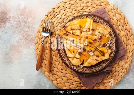 Crepes suzette con arance e cioccolato. Crepes sottile con cioccolato spalmato, nocciole e fette d'arancia frutta in piatto per colazione su cemento vecchio Foto Stock