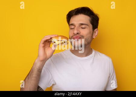 Assaggiato Guy entusiasta mangiare gustoso Burger allo Studio Foto Stock