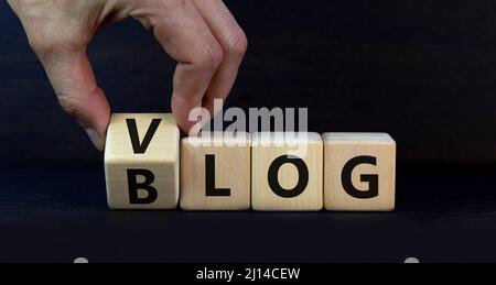 Simbolo blog o Vlog. Businessman trasforma i cubi di legno e cambia la parola Blog in Vlog. Bello sfondo grigio tavolo. Affari e informazioni Foto Stock