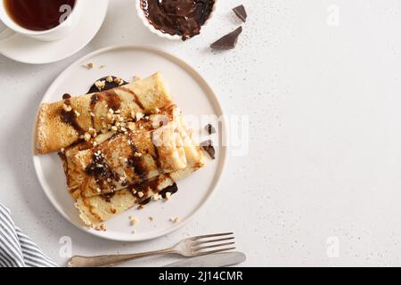 Pancake russi sottili con aggiunta di cioccolato e noci su sfondo bianco. Colazione tradizionale. Vista dall'alto. Spazio di copia. Cucina Ucraina. Foto Stock