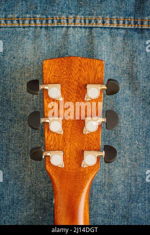 Il collo della chitarra acustica è in primo piano sul tessuto in denim. Cultura hipster. Sfondo. Strumento musicale. Imparare a suonare la chitarra. Foto Stock