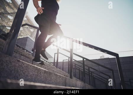 Vista ritagliata delle gambe dell'uomo sane e dai capelli grigi che scendono al piano inferiore e che si allenano all'aperto in centro in primavera Foto Stock