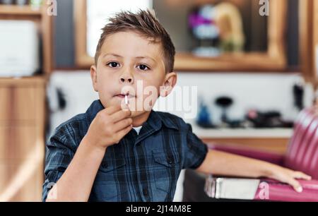 Oggi ho una nuova acconciatura dolce. Ritratto di un ragazzo adorabile che mangia un lecca-lecca dopo aver ottenuto un taglio di capelli fresco in un salone. Foto Stock