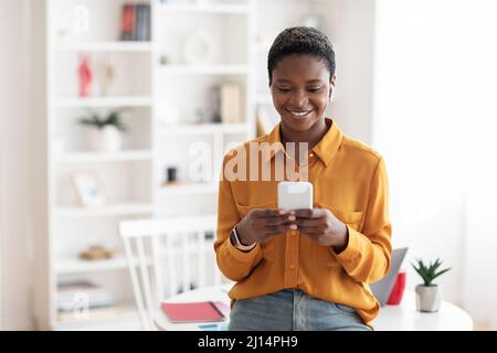 Giovane donna d'affari che utilizza gli auricolari più recenti e il telefono cellulare a casa Foto Stock
