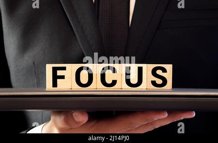 Uomo d'affari con segno Focus scritto su blocchi di legno bianco sul tavolo di fronte a lui Foto Stock