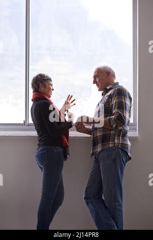 Conversazioni di coppia. Scatto di una coppia anziana che ha una discussione davanti ad una finestra. Foto Stock