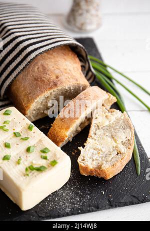 Pane fatto in casa di farina di grano appena sfornato di pane con burro e blocco di burro accanto ad esso su tavola di servizio di pietra nera in cucina casa. Foto Stock