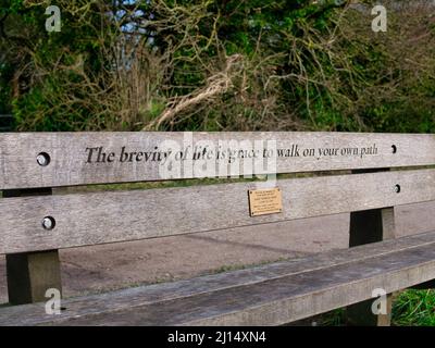 Un'iscrizione commemorativa su una panchina di legno recita 'la brevità della vita è la grazia di camminare sul vostro cammino'. Preso sul sentiero Wirral Way Walking nel Regno Unito Foto Stock