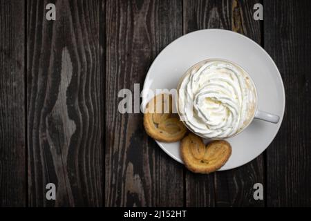 bevanda calda caffè o tè con panna montata con biscotti a forma di cuore su sfondo di legno scuro spazio copia, piatto Foto Stock