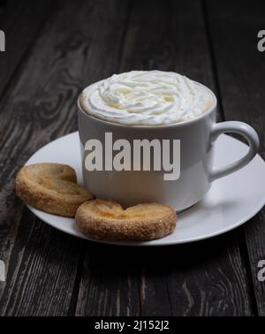 bevanda calda caffè o tè con panna montata con biscotti a forma di cuore su sfondo di legno scuro Foto Stock