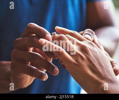 La sua celebrazione dell'amore eterno. Primo piano di un uomo irriconoscibile che mette un anello di fidanzamento sul suo dito fidanzato. Foto Stock